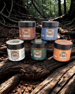 Wszystkie warianty maseł do brody Brodaty Ślązak ustawione na tle naturalnego krajobrazu – zielony las i leśne rośliny w tle